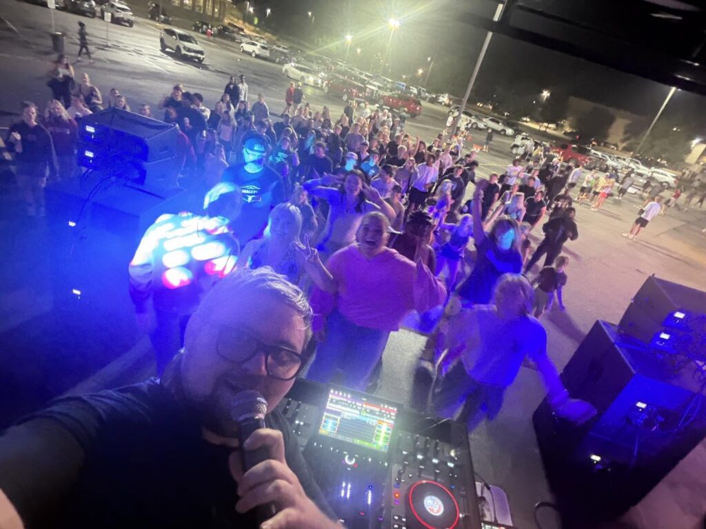 DJ at the controller with a large crowd behind him at an outdoor college event