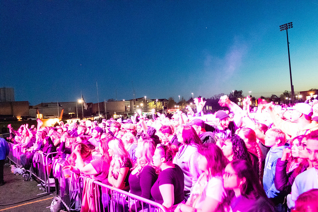 A large concert crowd lit by stage lighting at dusk