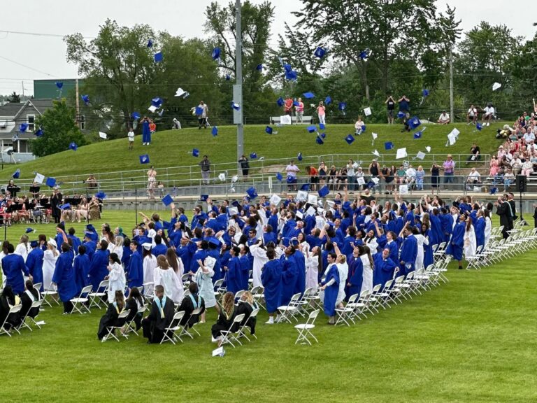 Graduates in blue gowns gathered on the field after a commencement ceremony