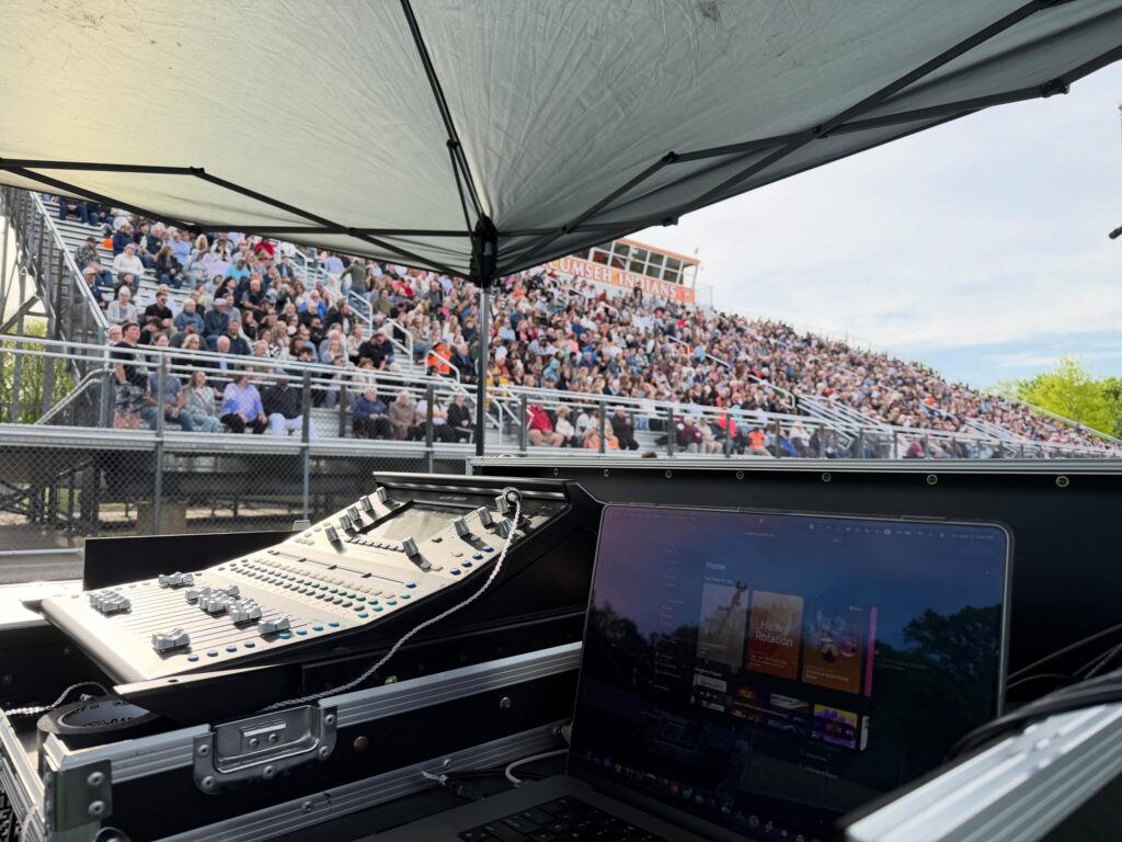Mixing console under a canopy facing a full grandstand at an outdoor commencement