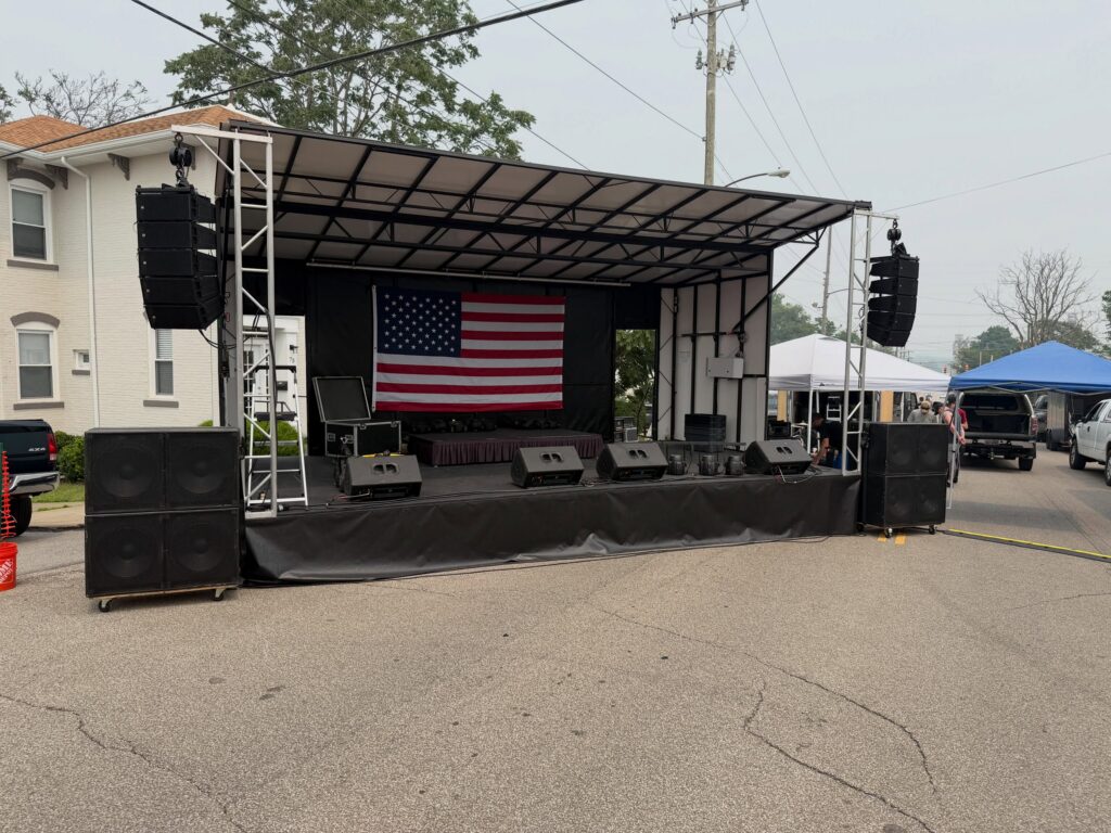 Mobile stage with a line array hung at stage left and a flag backdrop