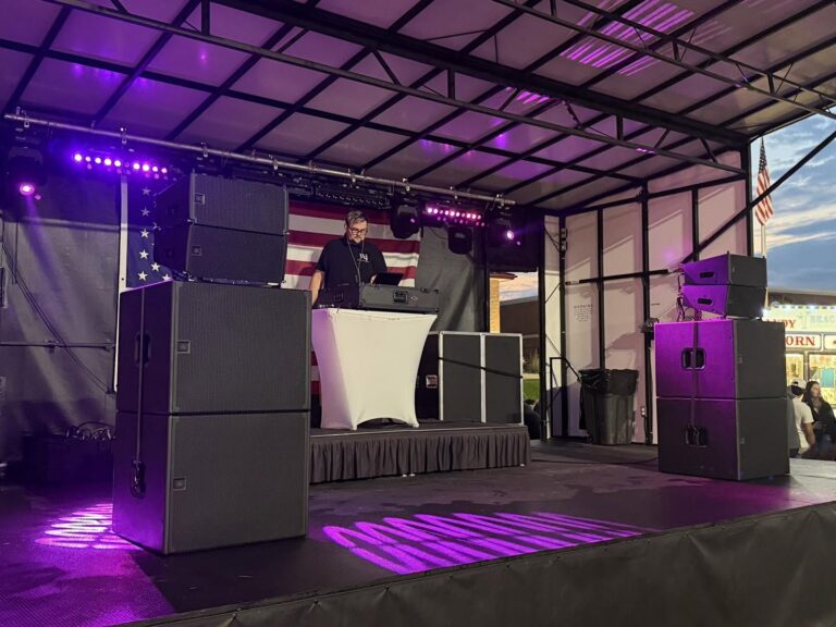 Mobile stage with purple lighting and speaker stacks at dusk