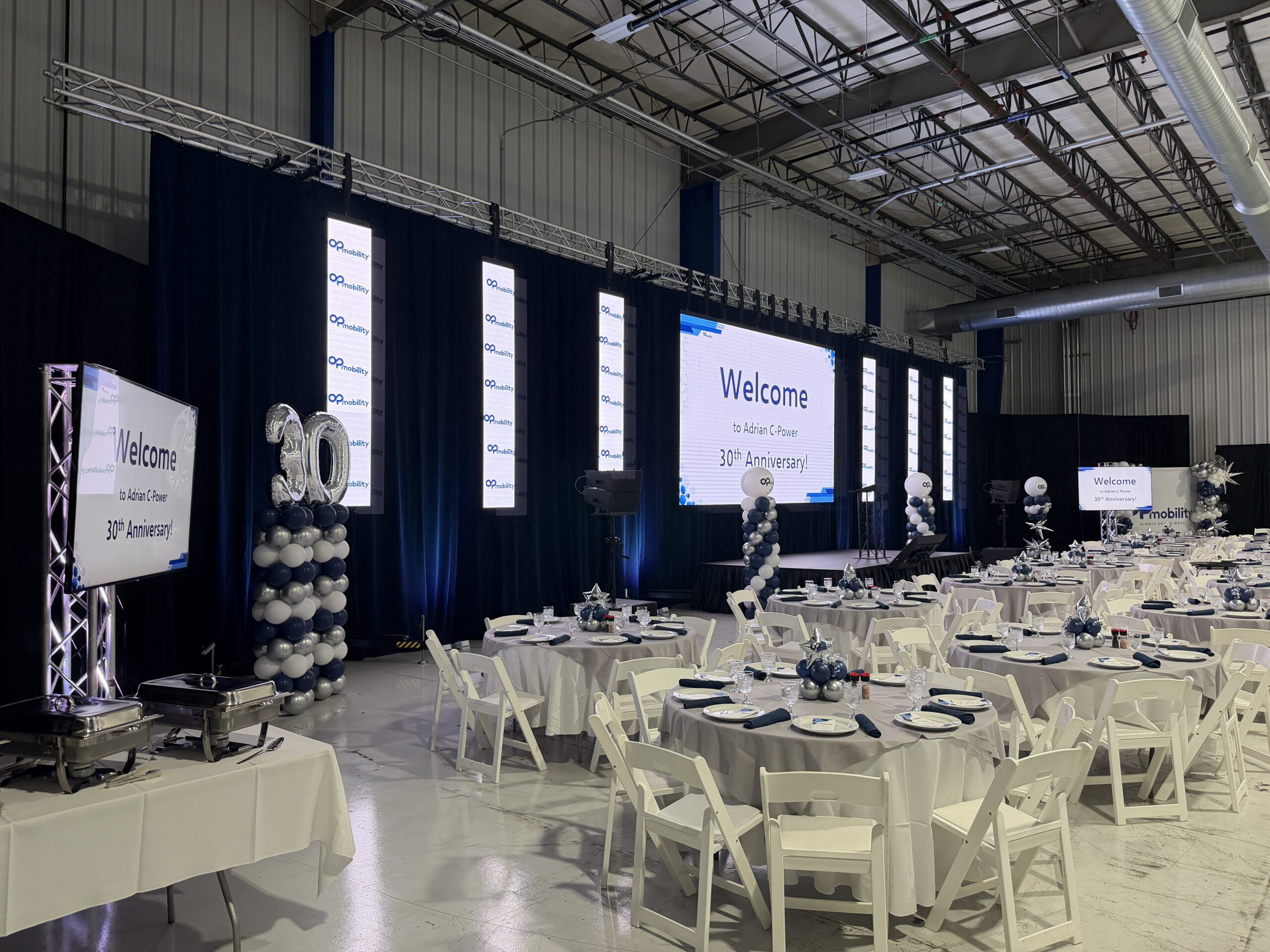 Banquet tables facing an LED video wall, LED columns and relay screens at the OPmobility 30th anniversary celebration in Adrian