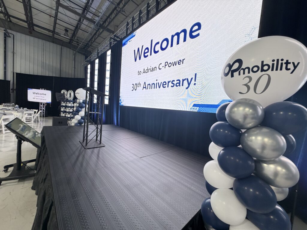 LED video wall reading Welcome to Adrian C-Power 30th Anniversary, above a stage with a lectern