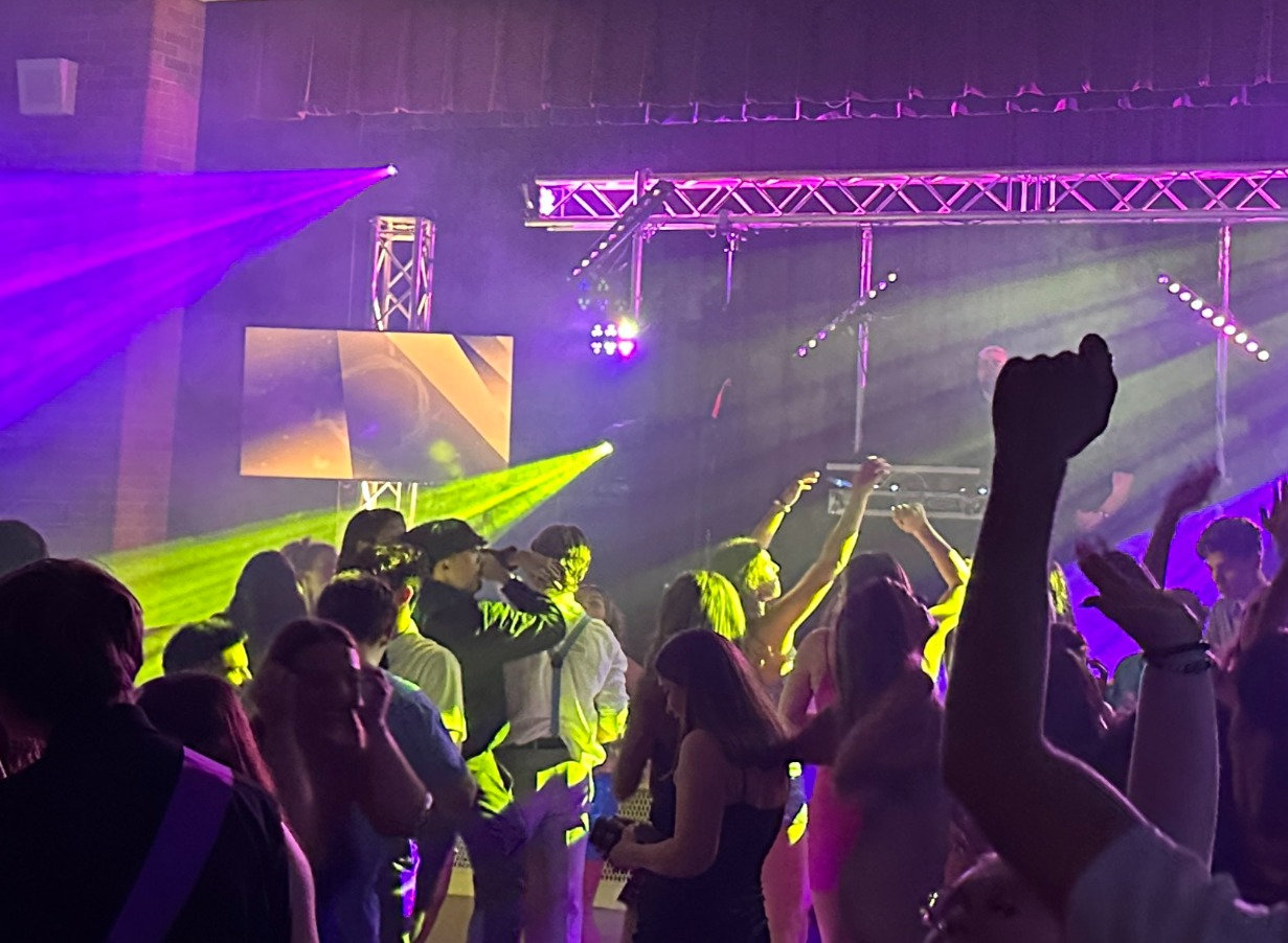 Dance floor packed with guests under purple and green beams from a truss rig