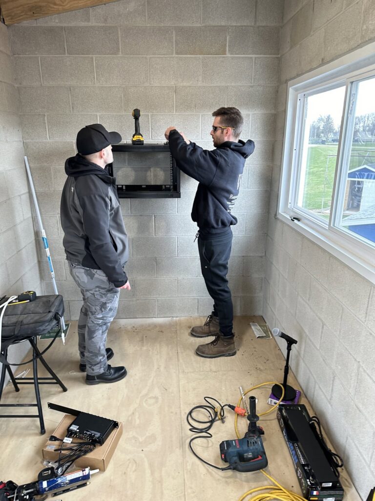 Two technicians installing audio equipment in a room