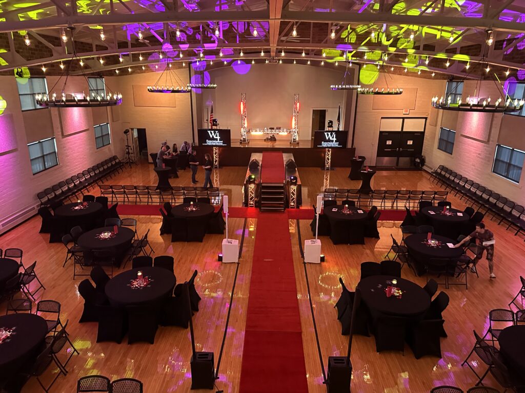 The Adrian Armory hall set for a prom, seen from the balcony: round tables, a red carpet down the middle and the stage lit at the far end.